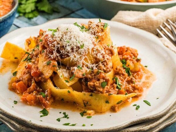 Pasta topped with authentic Bolognese sauce and grated cheese, served on a white plate with a parsley garnish.