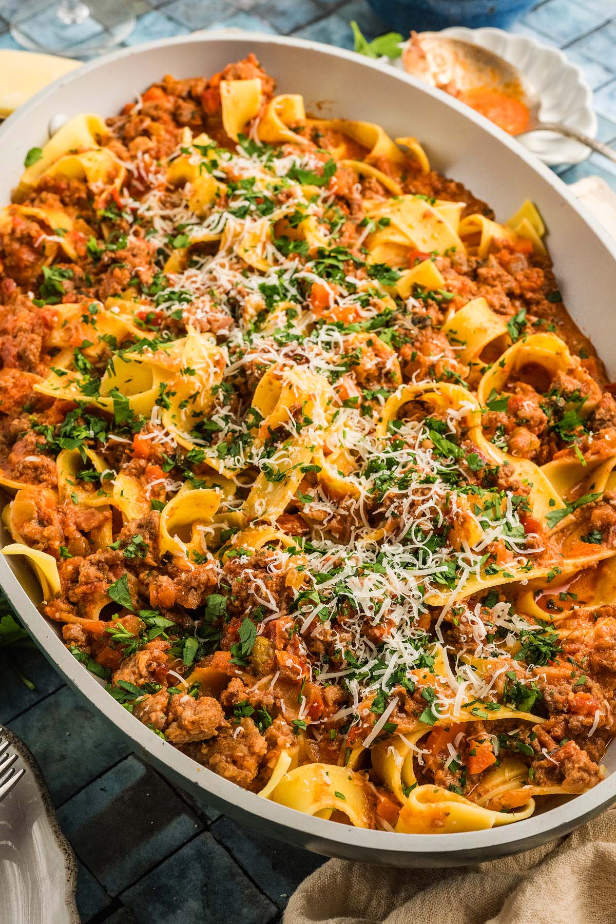 Wide pan of pappardelle pasta with authentic Bolognese sauce, topped with grated cheese and chopped parsley.