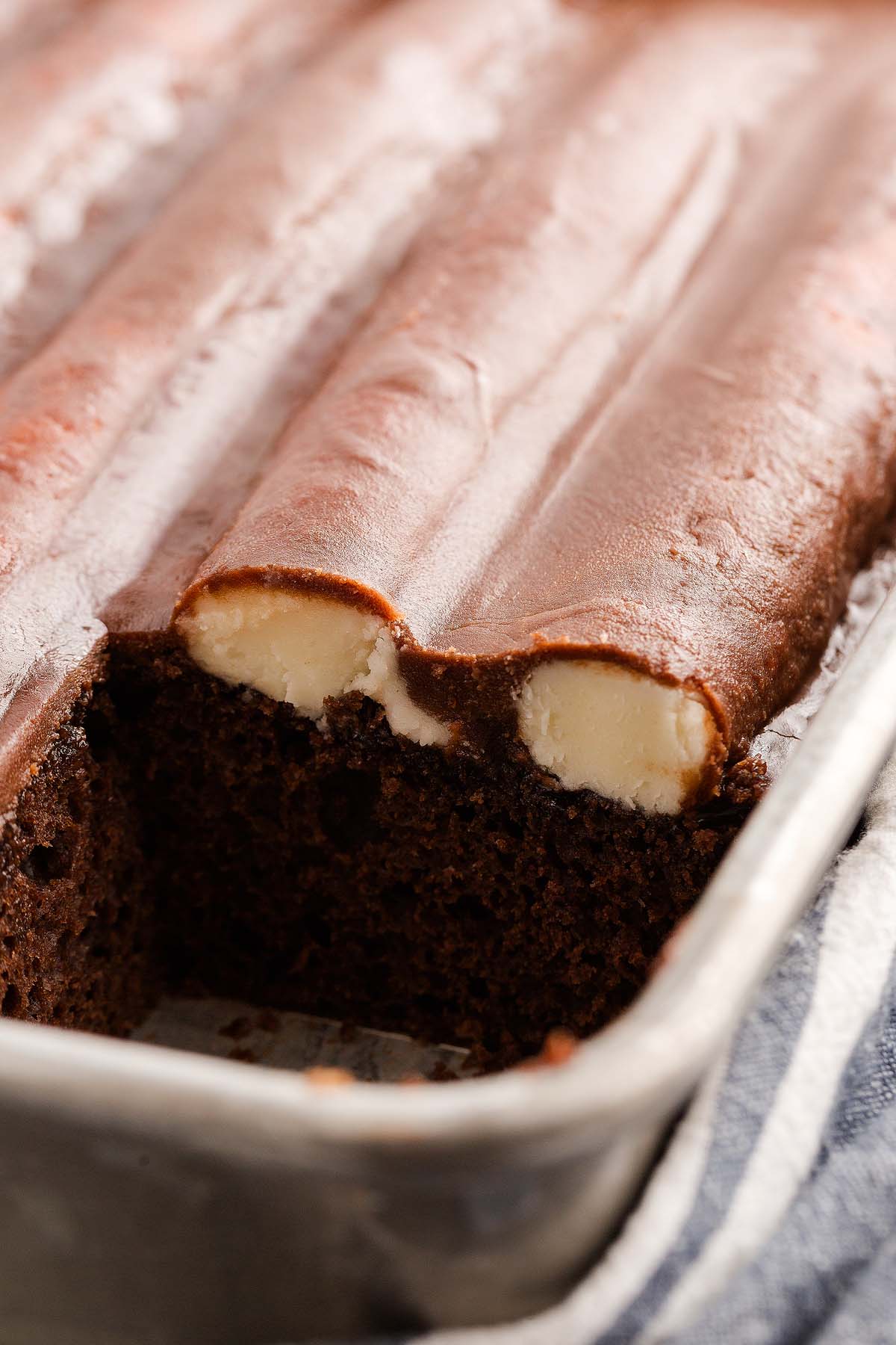 Chocolate bumpy cake sheet cake with creamy filling, partially sliced in a metal pan, frosting on top, close-up view.