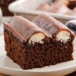A slice of bumpy cake with a creamy filling sits on a white plate, accompanied by a fork and napkin.