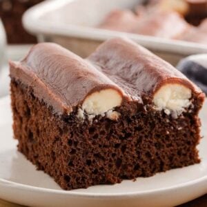 A slice of bumpy cake with a creamy filling sits on a white plate, accompanied by a fork and napkin.