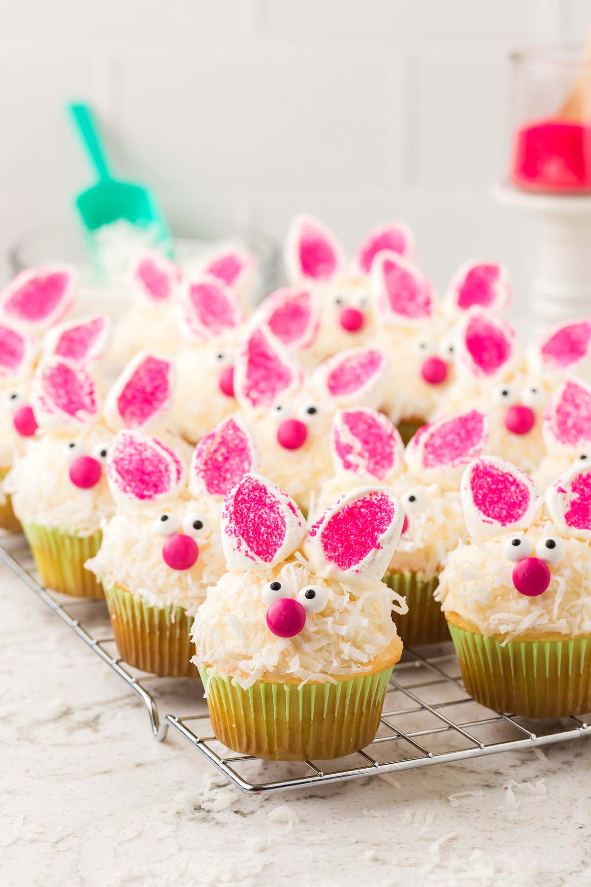 Adorable bunny cupcakes with pink ears, candy eyes, and noses are displayed on a cooling rack, ready to delight any sweet tooth.