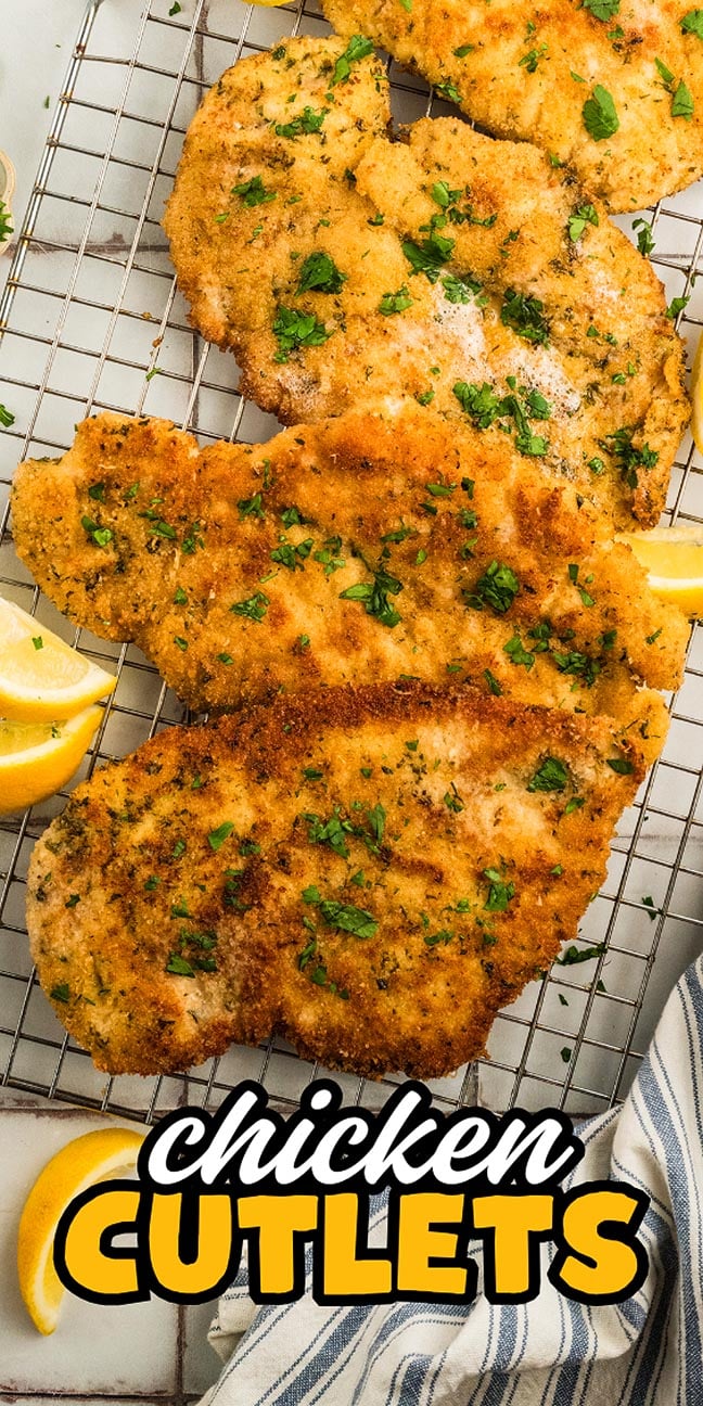 Crispy golden chicken cutlets rest on a cooling rack, garnished with fresh parsley, accompanied by lemon wedges and a striped napkin.