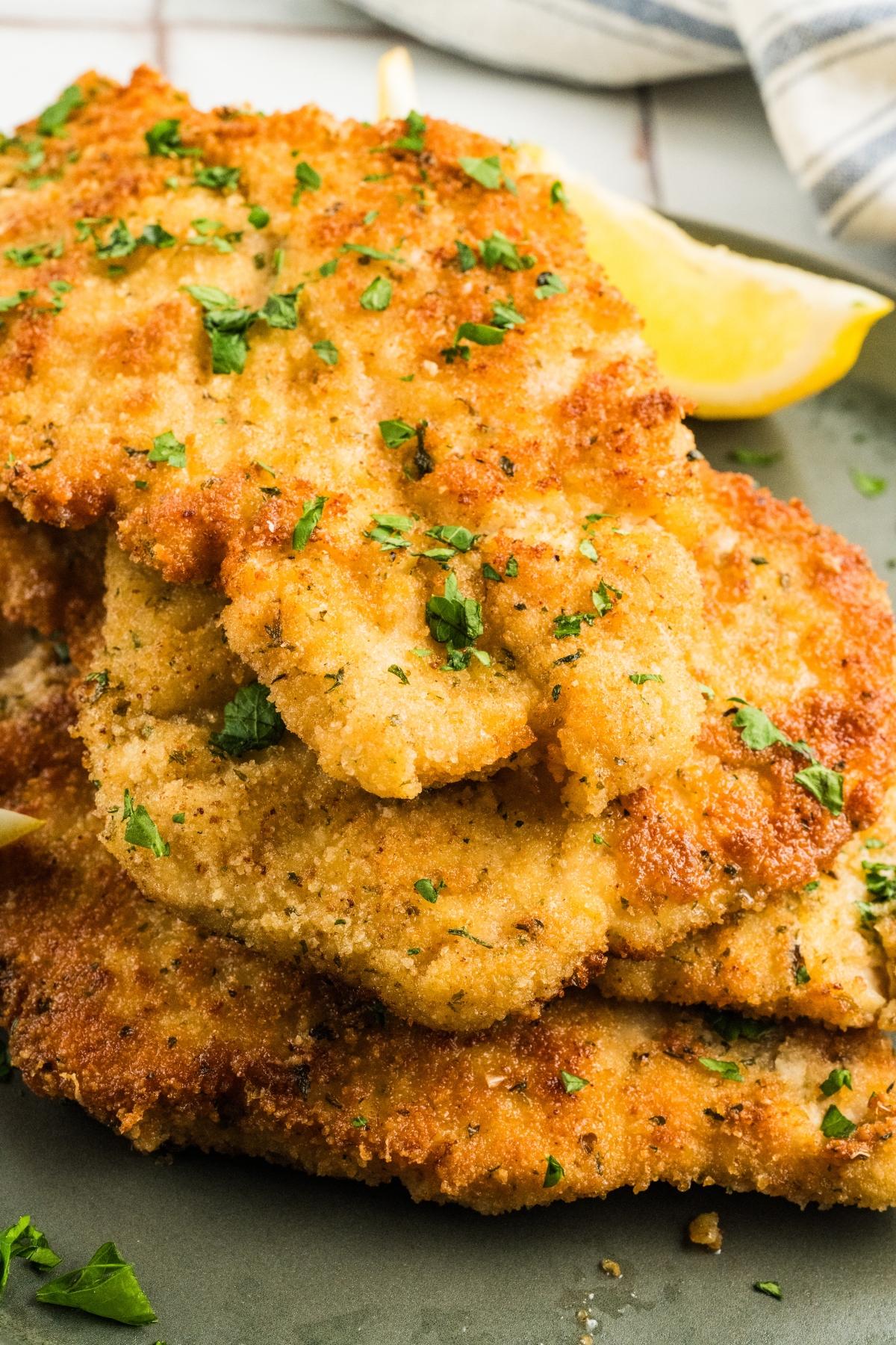 Golden brown breaded chicken cutlets garnished with chopped parsley, served with lemon wedges.