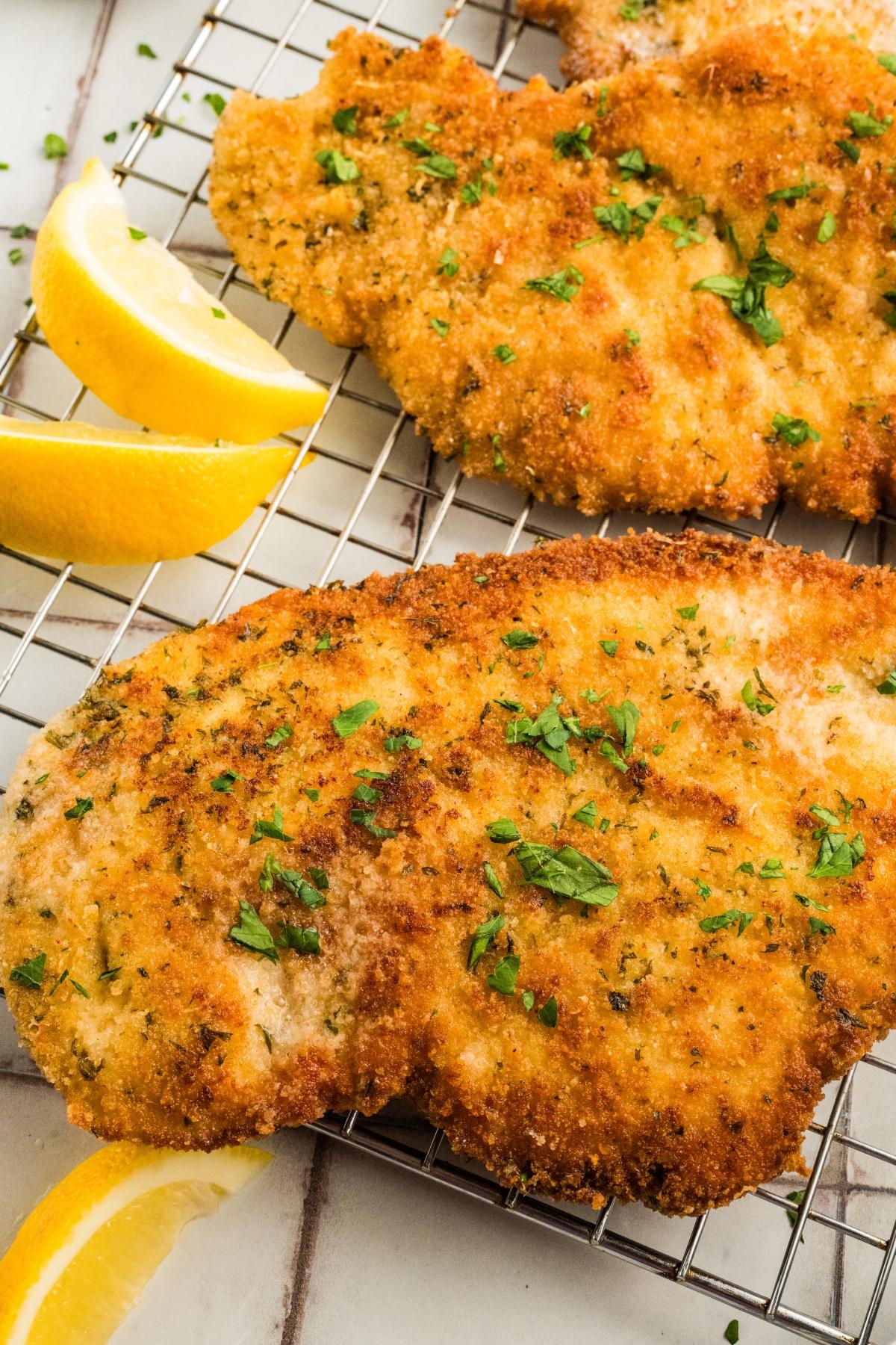 Golden breaded chicken cutlets garnished with parsley, served with lemon wedges on a cooling rack.