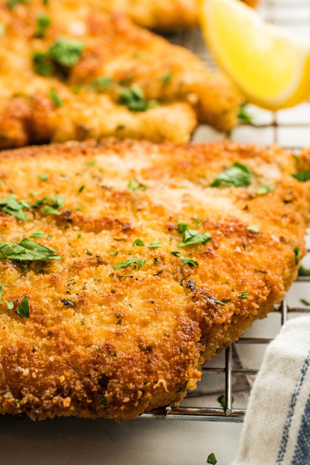 Close-up of a crispy breaded schnitzel garnished with chopped herbs and a lemon wedge in the background.