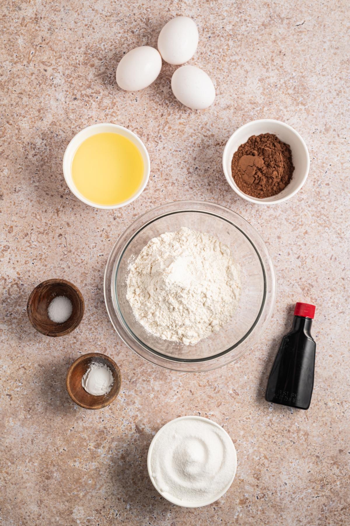 Baking ingredients, including eggs, flour, cocoa powder, sugar, melted butter, vanilla, salt, and baking soda.