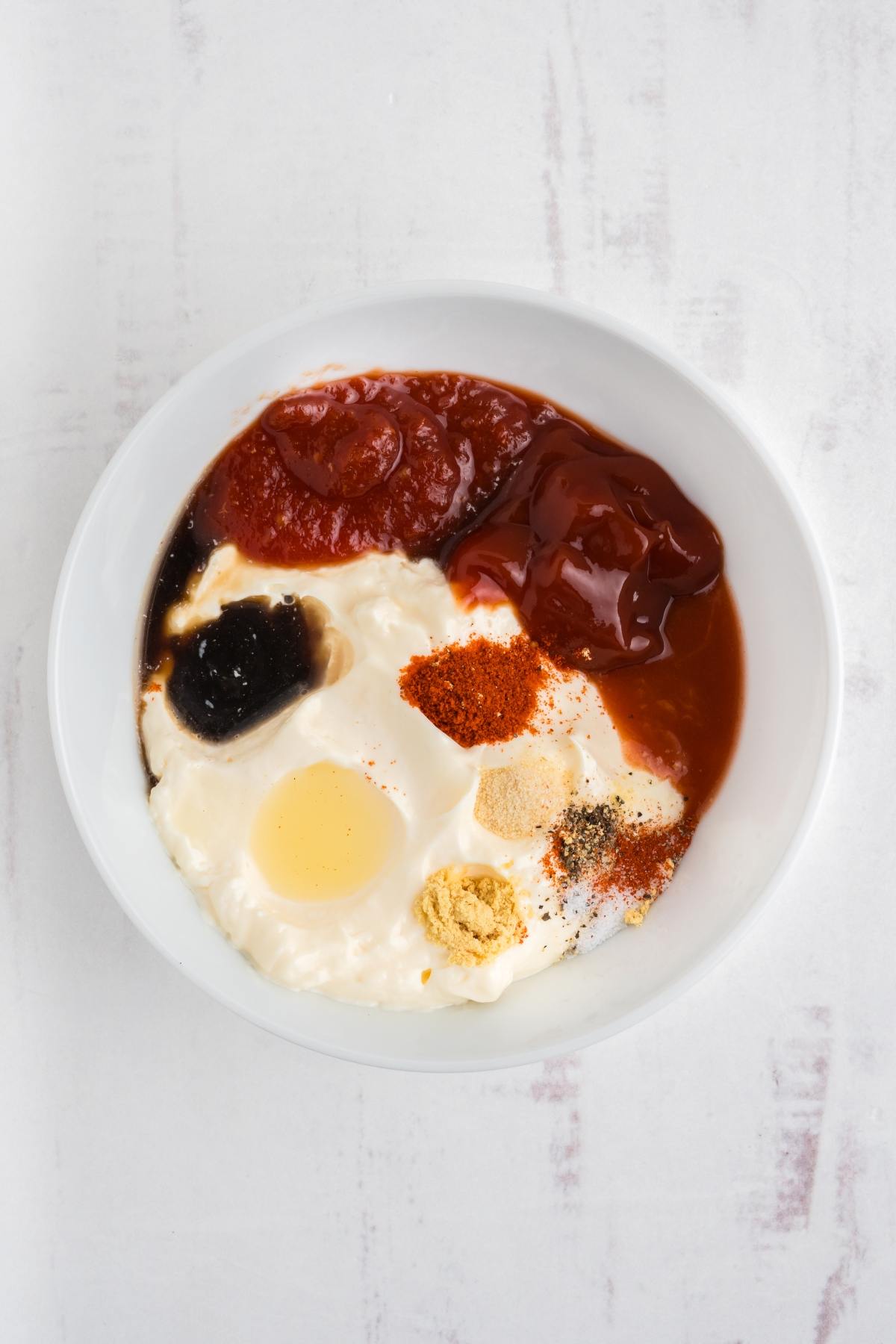 A white bowl with mayonnaise, ketchup, tomato sauce, spices, and a splash of Worcestershire sauce.