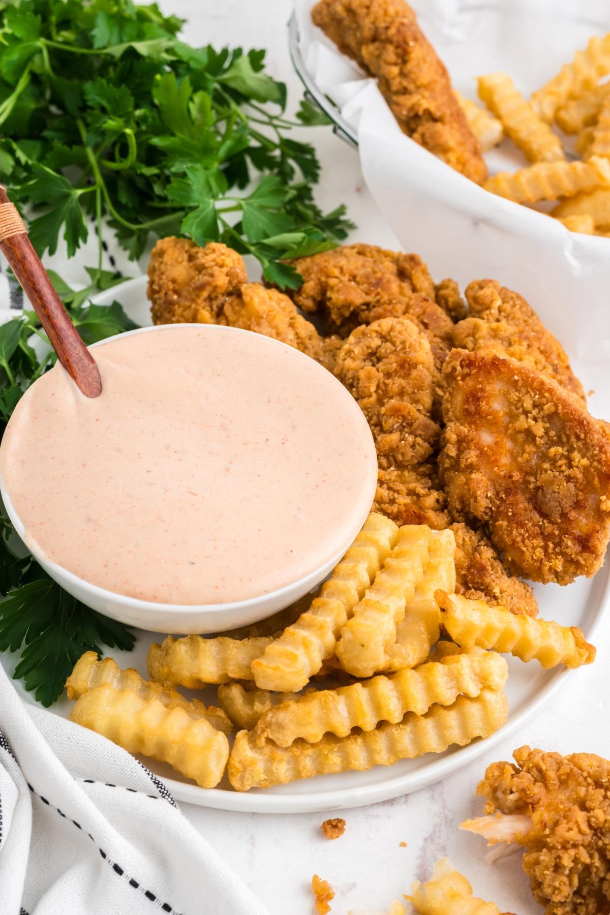 Plate of crinkle-cut fries, fried chicken tenders, and a bowl of dipping sauce with parsley garnish.