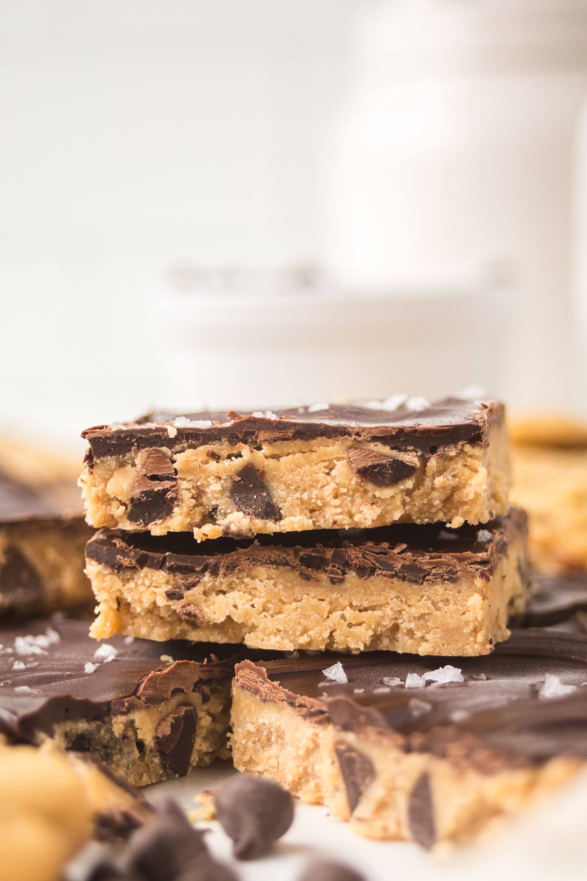 Three chocolate-topped cookie dough bars stacked on each other, with chocolate chips and sea salt visible.
