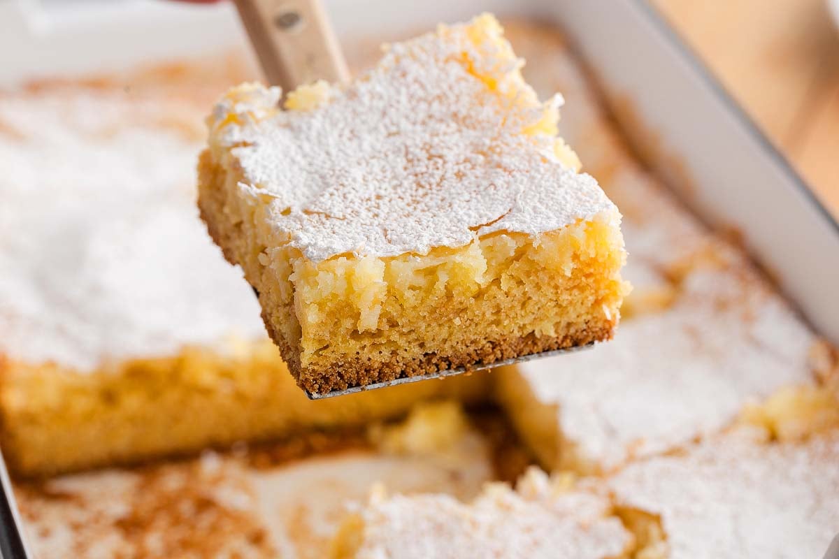 A gooey butter cake square, a classic St. Louis dessert&mdash;is dusted with powdered sugar and lifted from the baking dish, its rich layers perfectly revealed.