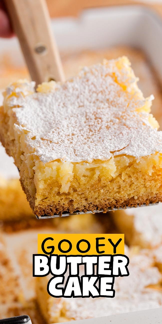 A close-up of a gooey butter cake slice topped with powdered sugar, being lifted from a pan, shows off the rich and irresistible texture of this classic dessert.