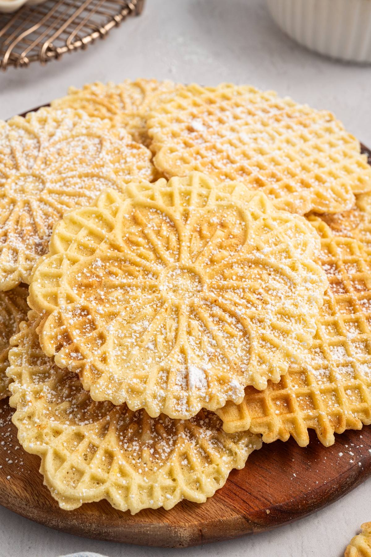 Several thin, round italian pizzelle cookies dusted with powdered sugar on a wooden board.