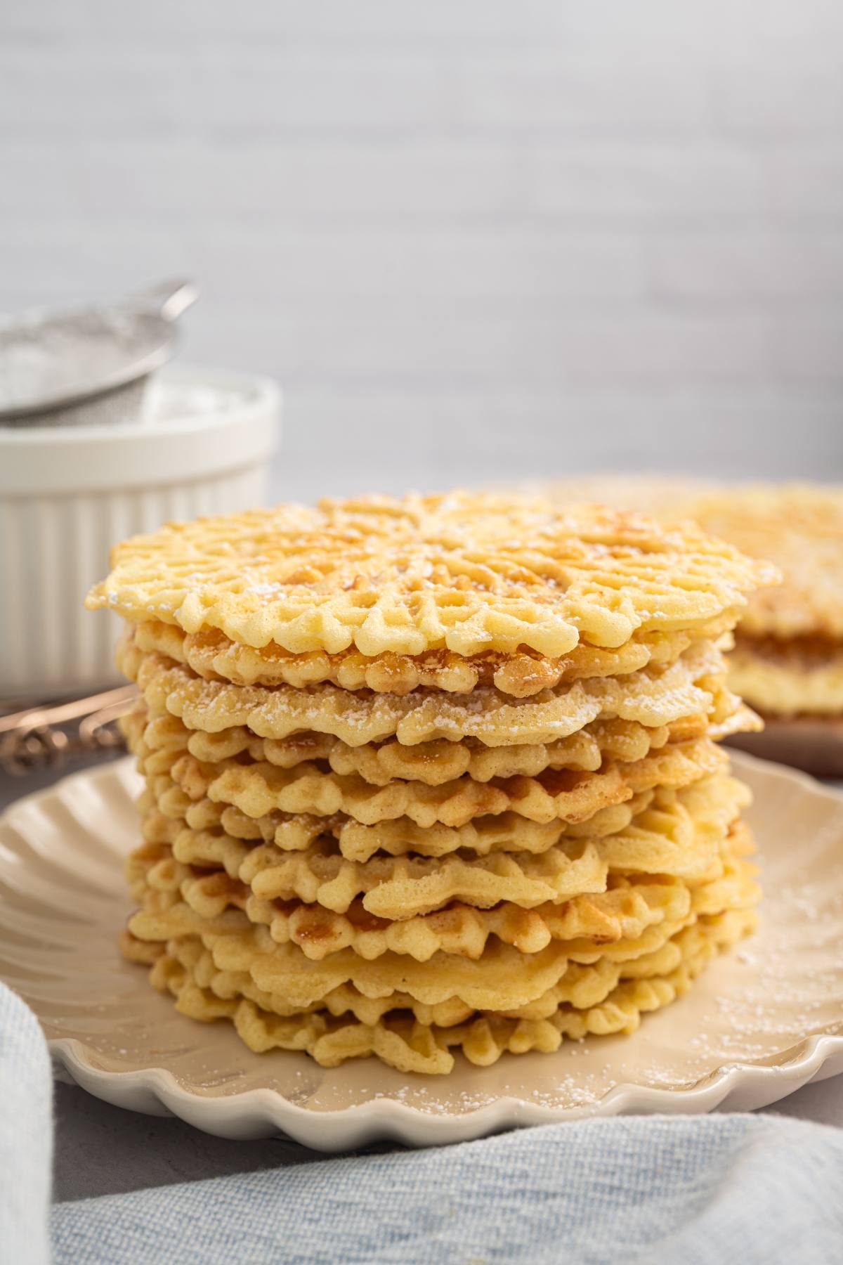 A stack of golden, crispy italian pizzelle cookies on a plate with a soft focus background.