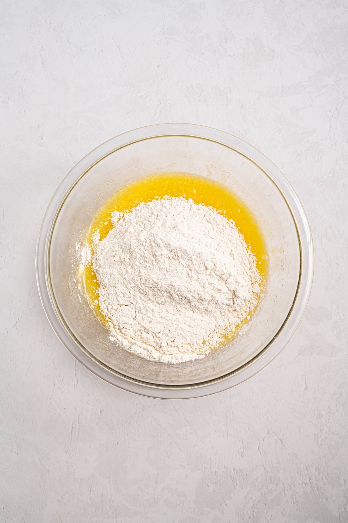 A glass bowl with flour on top of melted butter, set on a light-colored surface.