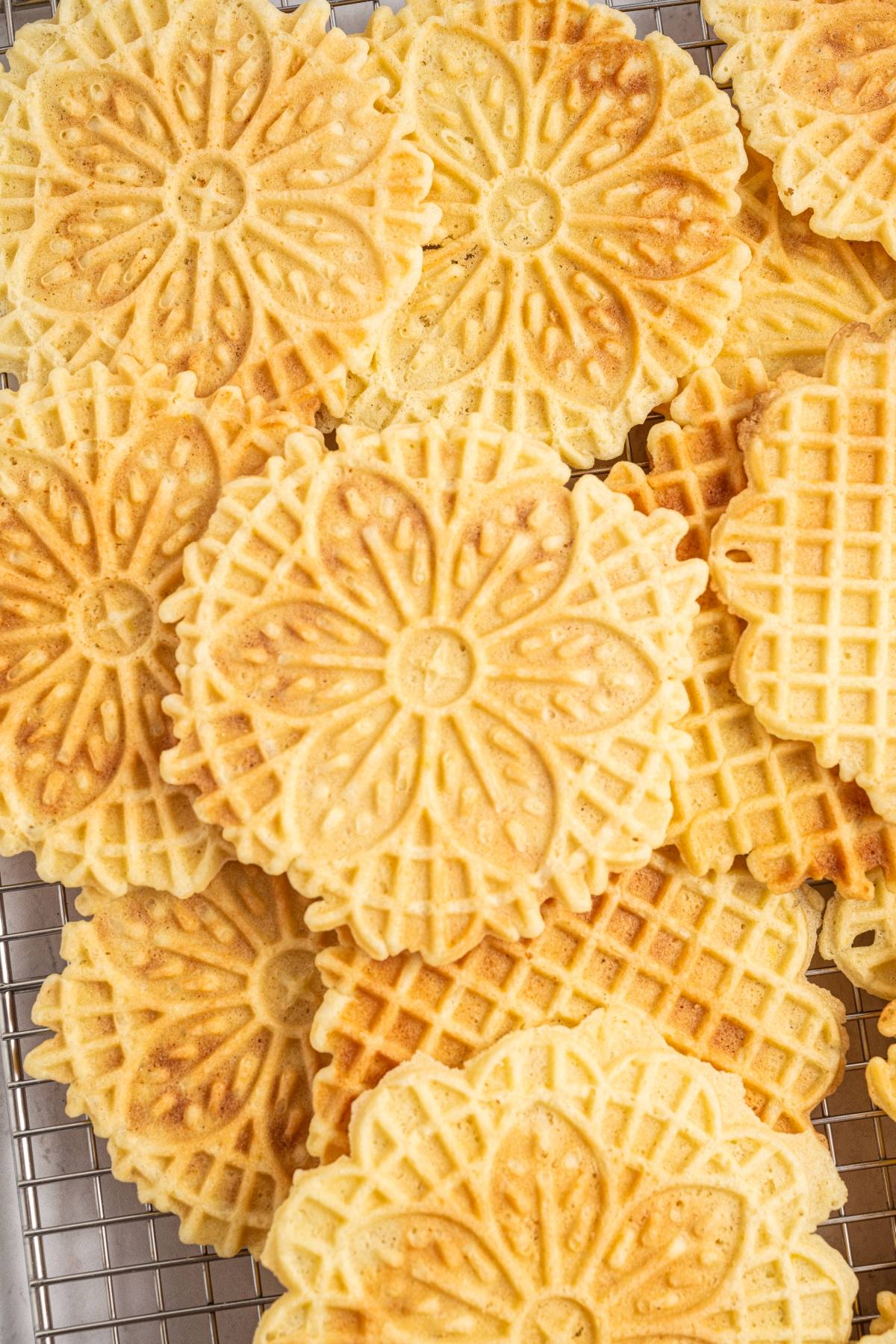Round, golden-brown italian pizzelle cookies with floral patterns stacked on a cooling rack.
