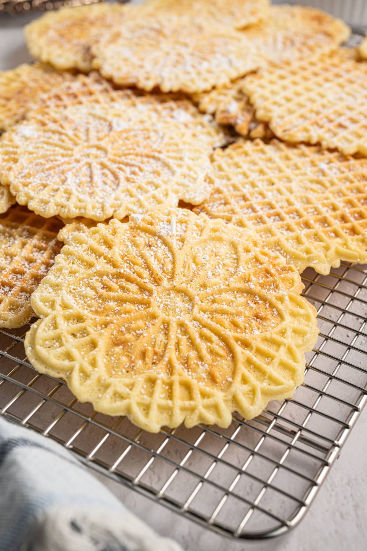 Round, golden italian pizzelle cookies dusted with powdered sugar, cooling on a metal wire rack.