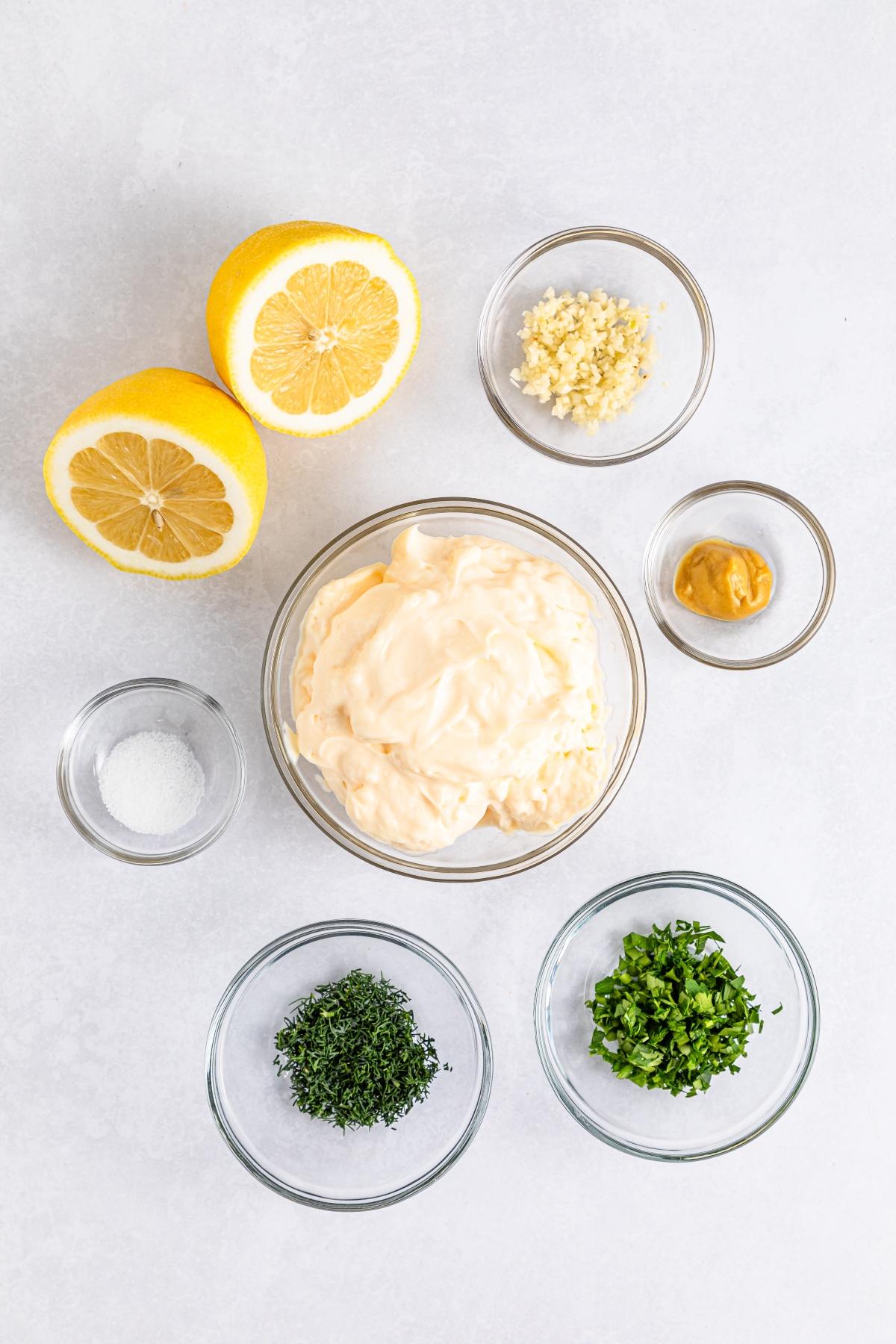 Ingredients for a sauce: mayo, lemon, garlic, mustard, salt, chopped parsley, and chopped dill in bowls.