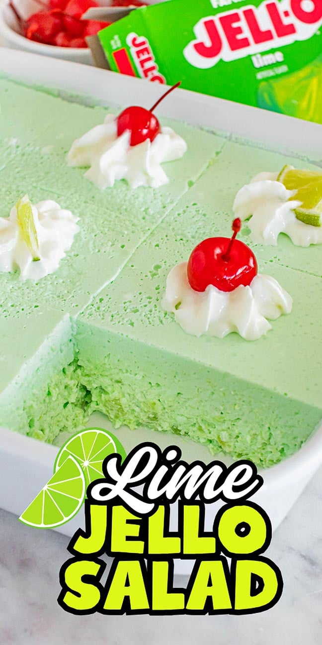 Lime Jello Salad topped with whipped cream, cherries, and fresh lime pieces served in a white dish.