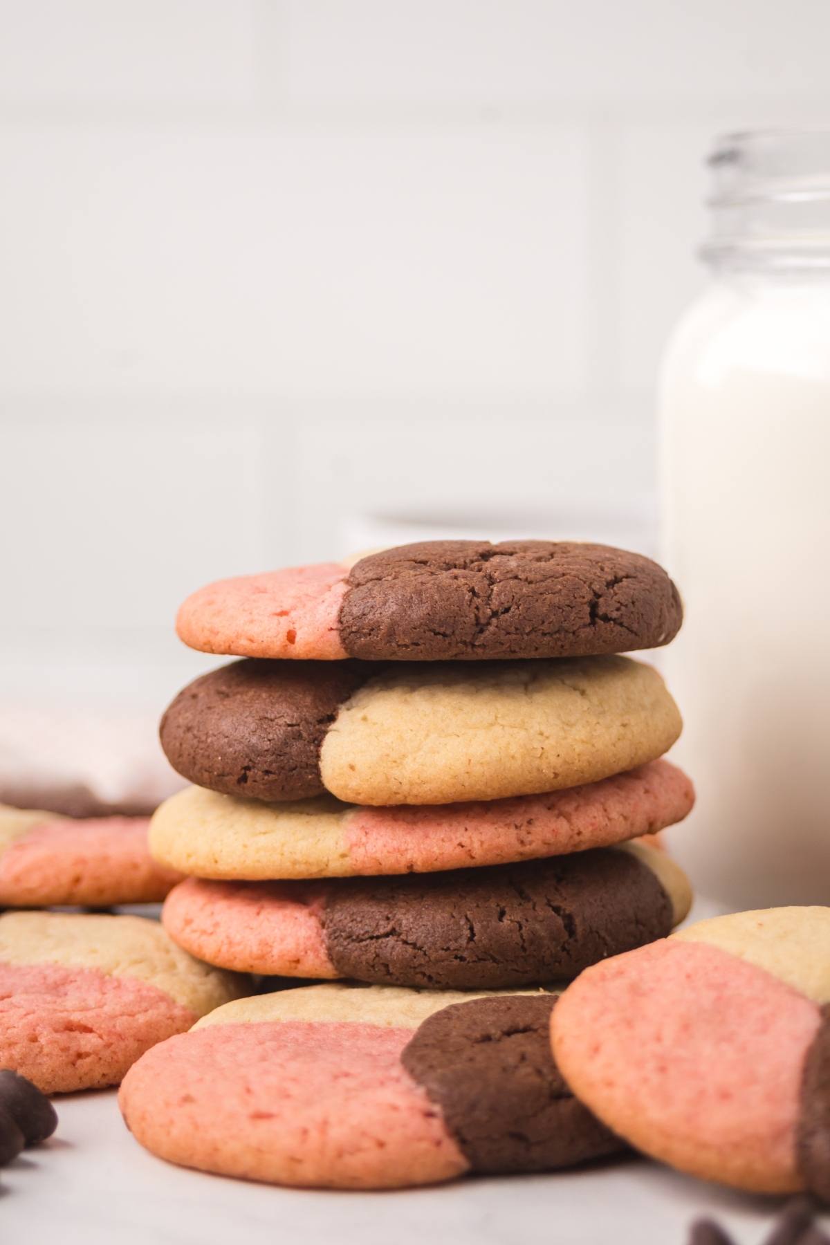 Stack of pink, brown, and beige neapolitan  cookies with a jar of milk in the background.