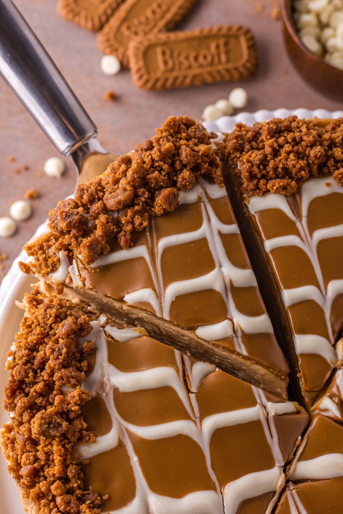 Close-up of a sliced no bake Biscoff cake with white icing drizzle and crumbled cookie topping.