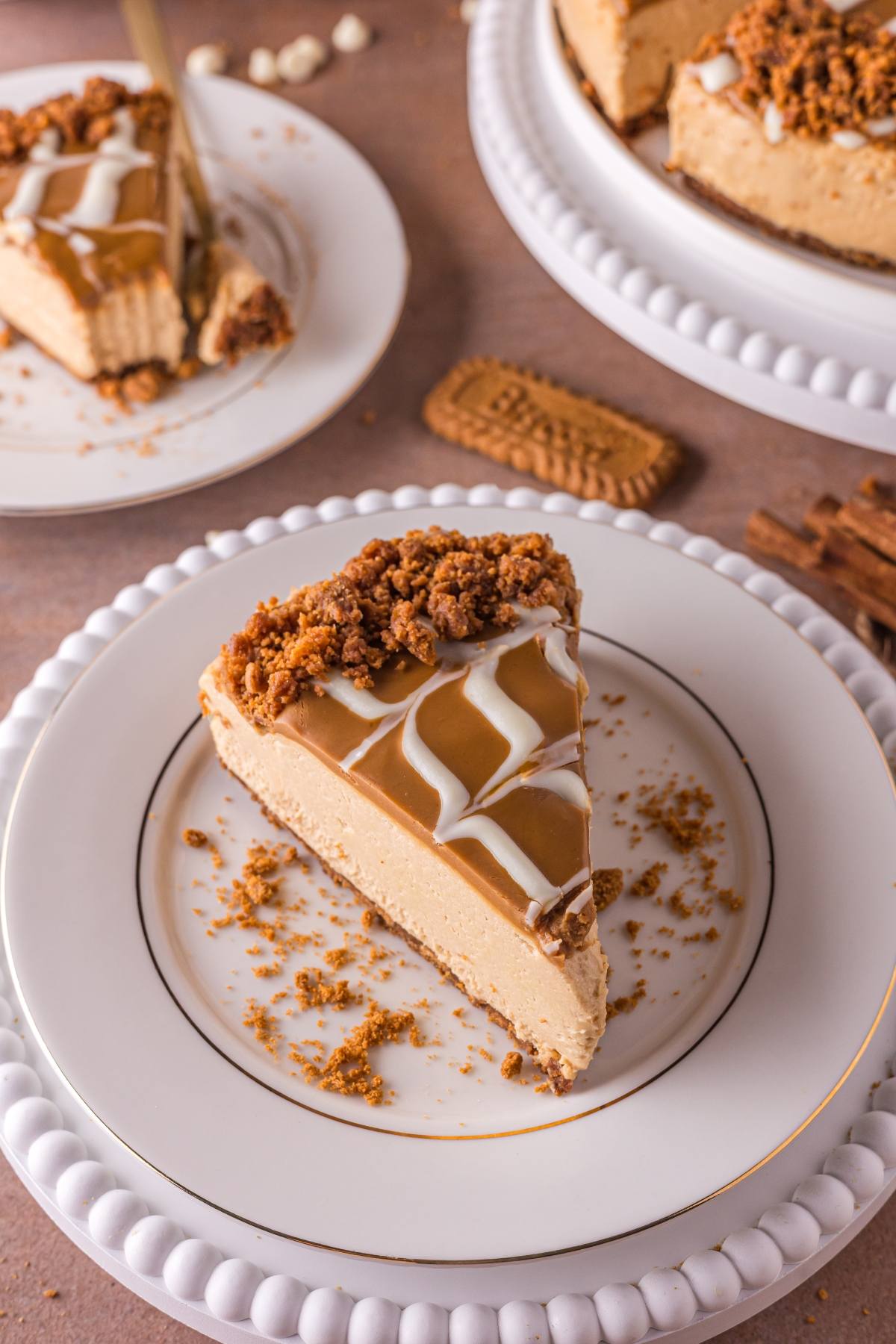A slice of no bake biscoff cheesecake with caramel topping and cookie crumbs on a white plate.