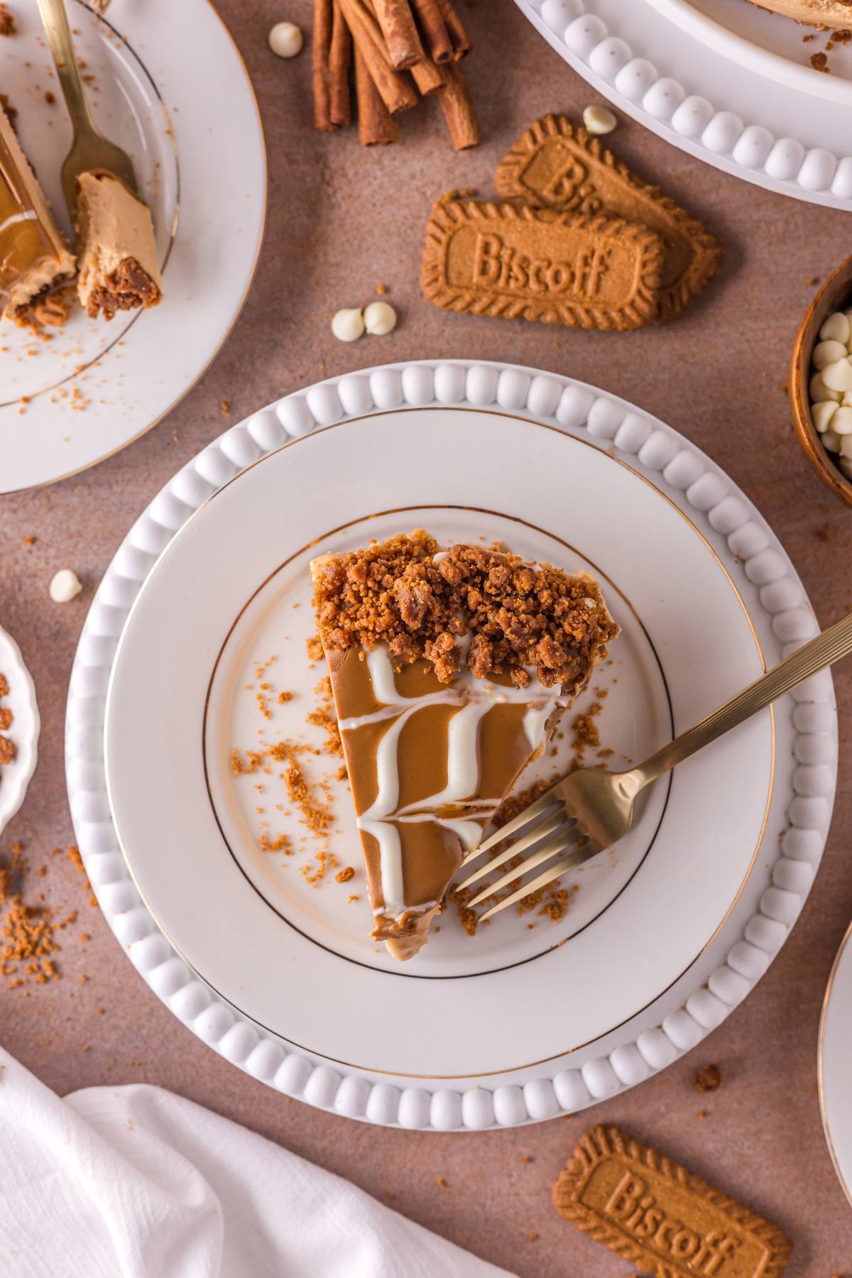 A slice of no bake Biscoff cheesecake on a plate with a fork, surrounded by cookies and cheesecake crumbs.