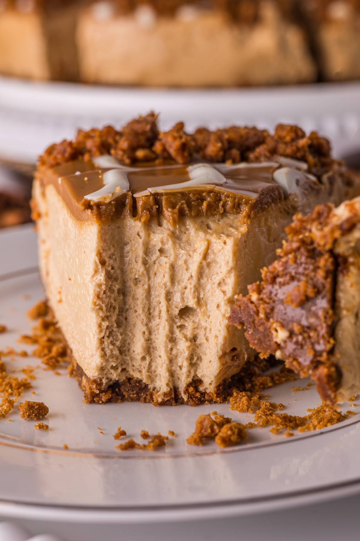 A slice of creamy no bake biscoff  cheesecake with a crumbly crust and caramel topping on a white plate.