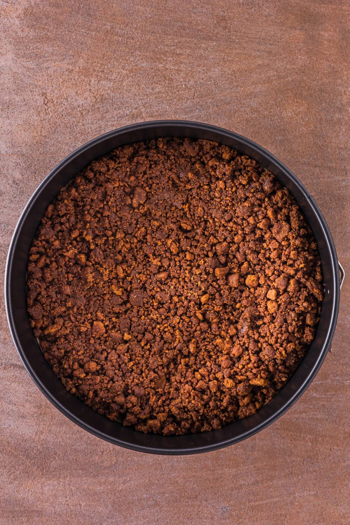 Overhead view of a round pan filled with a chocolate crumb crust on a brown surface.