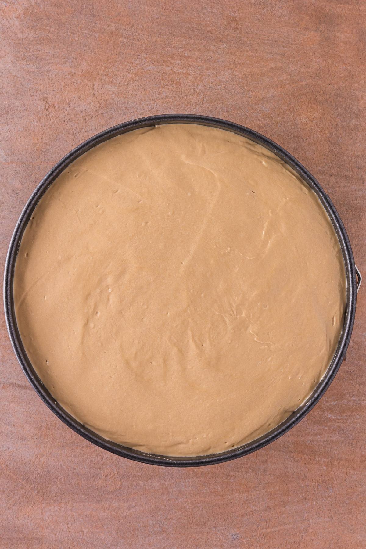 Round cake pan filled with smooth, light brown batter on a brown surface, ready for baking.