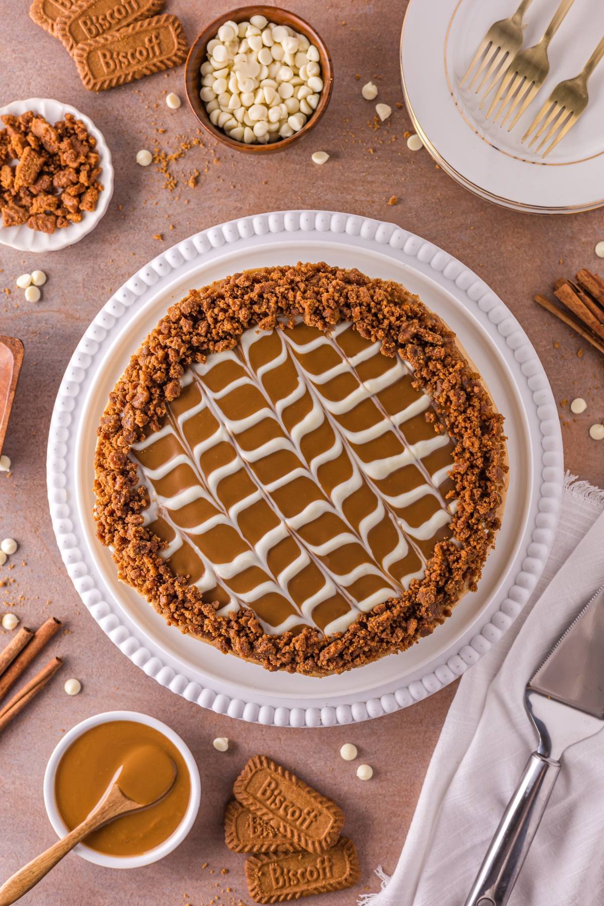 A Biscoff cheesecake with white and brown swirled topping, surrounded by cookies and white chocolate chips.