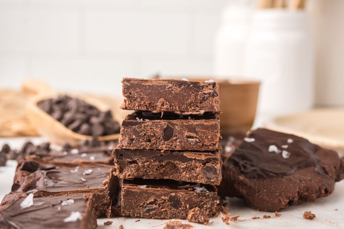 A stack of chocolate fudge brownies with sea salt on top, surrounded by chocolate chips&mdash;perfect inspiration for creating decadent no bake brownie bars at home.