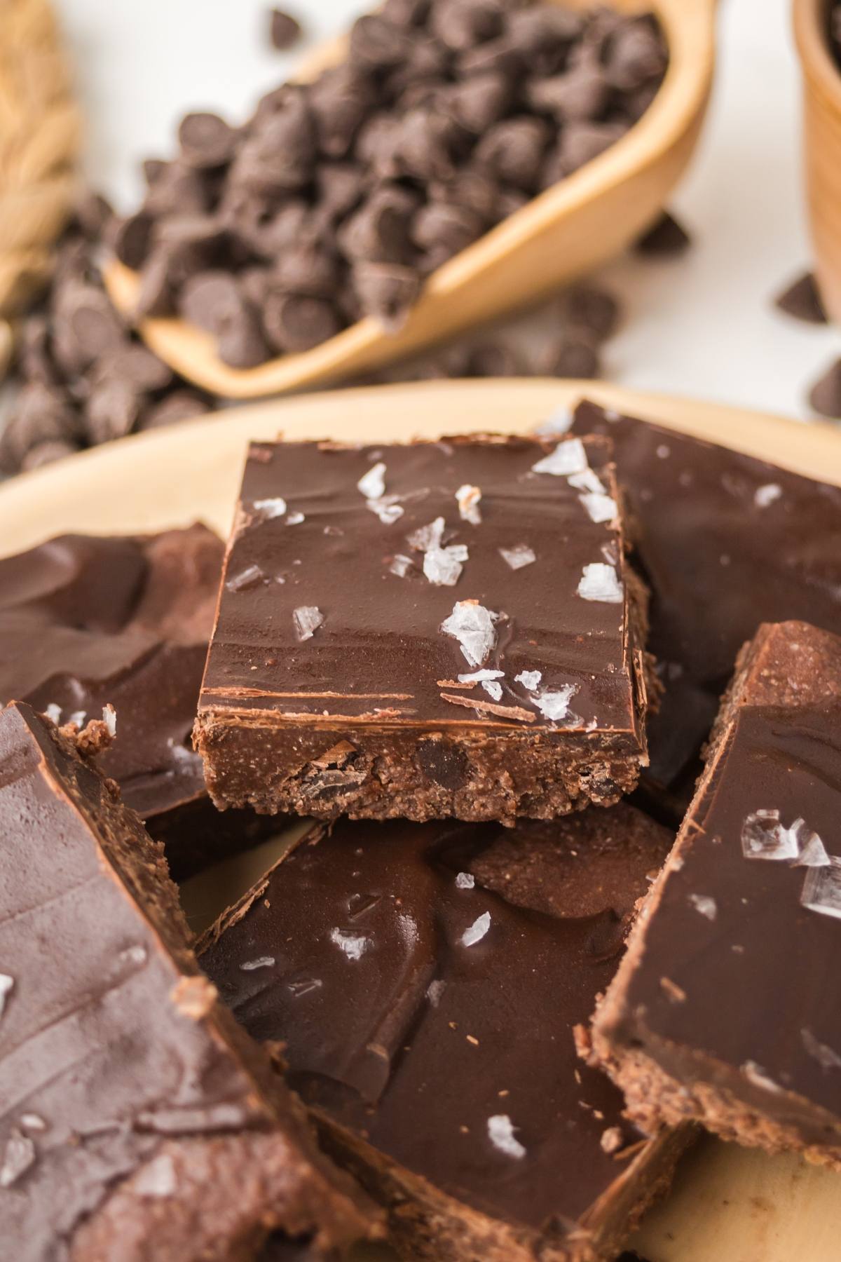Chocolate no bake brownie bars topped with sea salt flakes, with chocolate chips in the background.