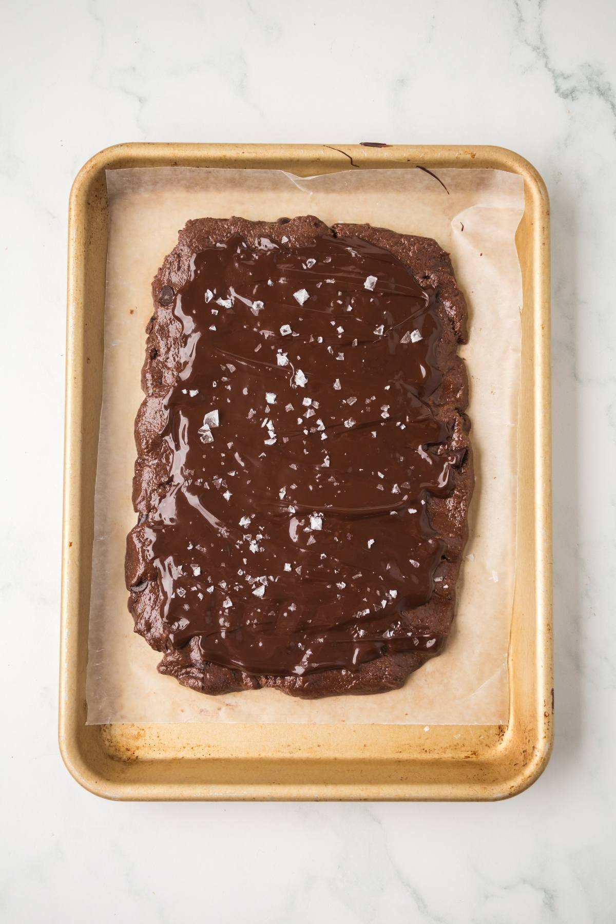 A chocolate slab topped with sea salt on parchment paper in a baking tray.