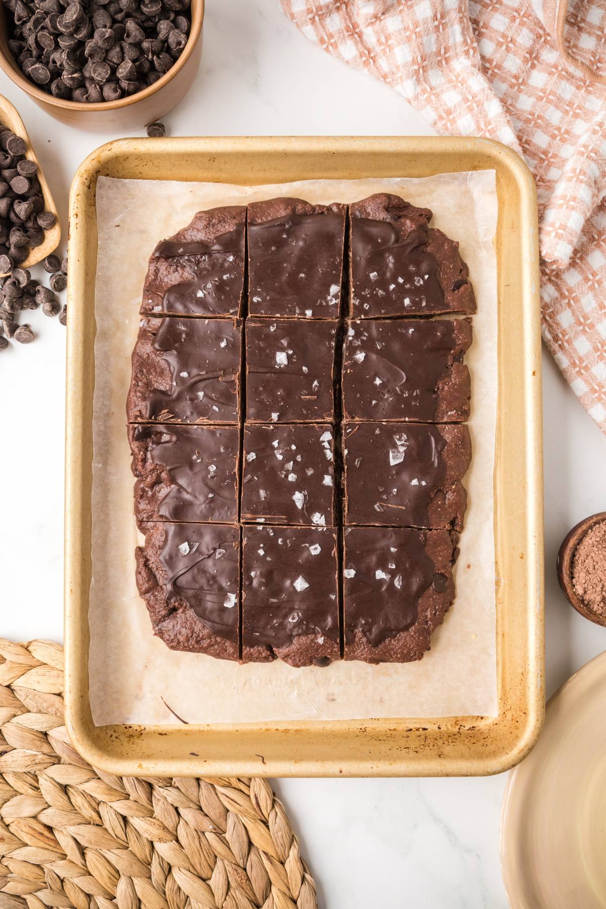 A tray of chocolate brownies cut into squares, topped with sea salt, on parchment paper.
