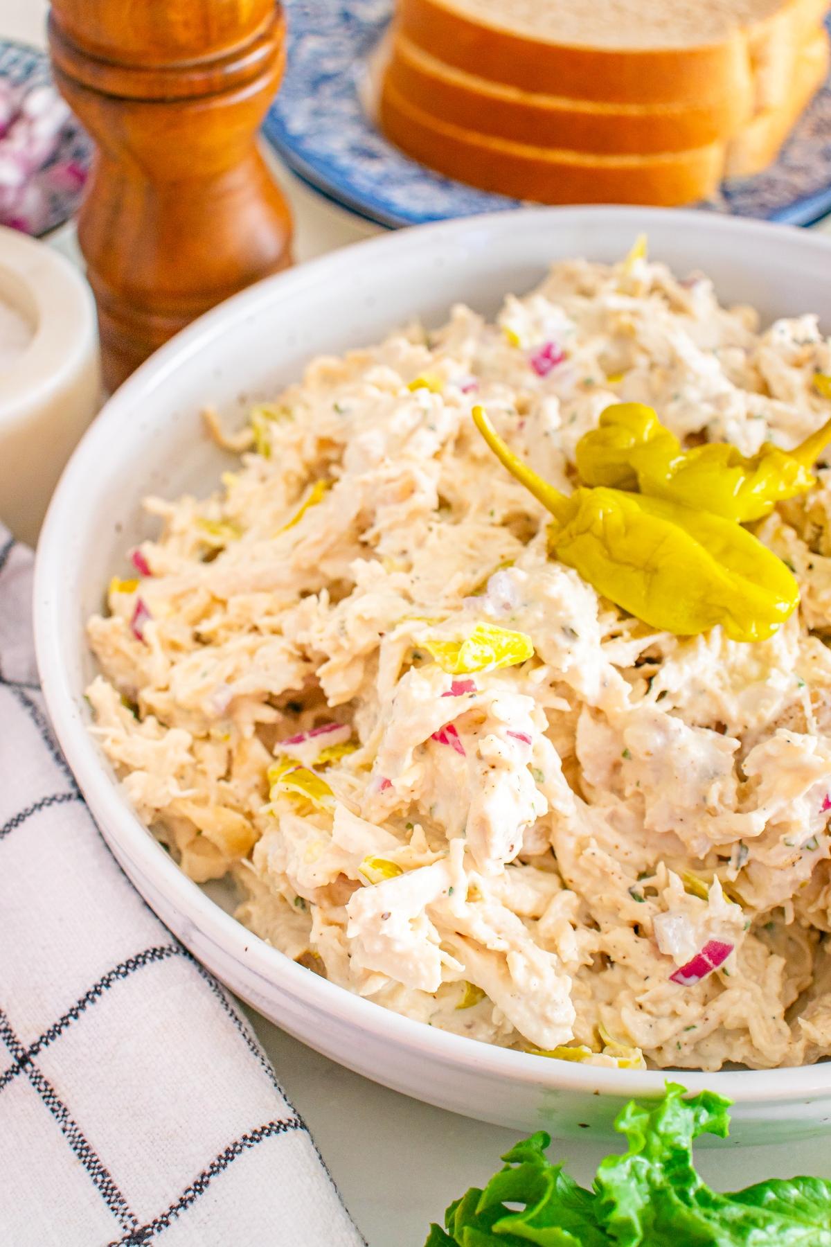A bowl of creamy chicken salad with sliced red onions and a whole pepperoncini on top.