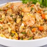 A plate of Shrimp Fried Rice with diced carrots, egg, and greens, garnished with fresh lettuce.