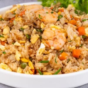 A plate of Shrimp Fried Rice with diced carrots, egg, and greens, garnished with fresh lettuce.