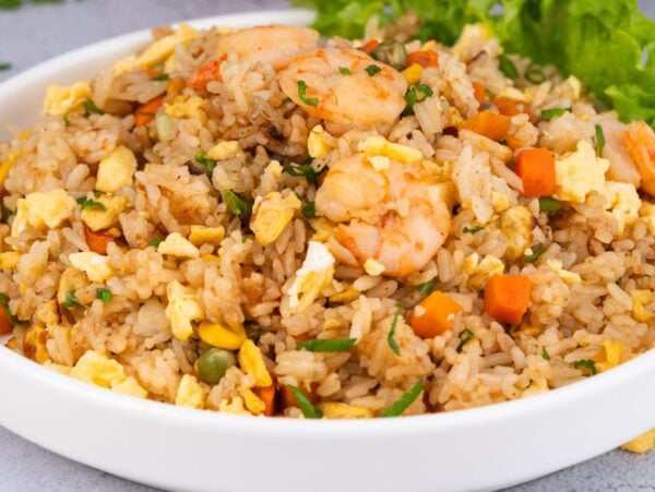 A plate of Shrimp Fried Rice with diced carrots, egg, and greens, garnished with fresh lettuce.