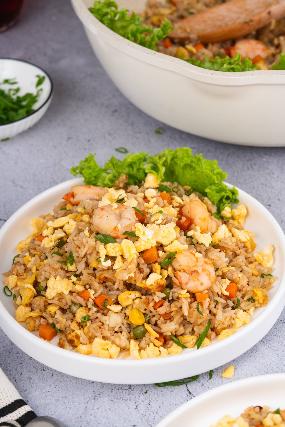 A plate of shrimp fried rice with scrambled eggs, vegetables, and lettuce garnish on a gray surface.