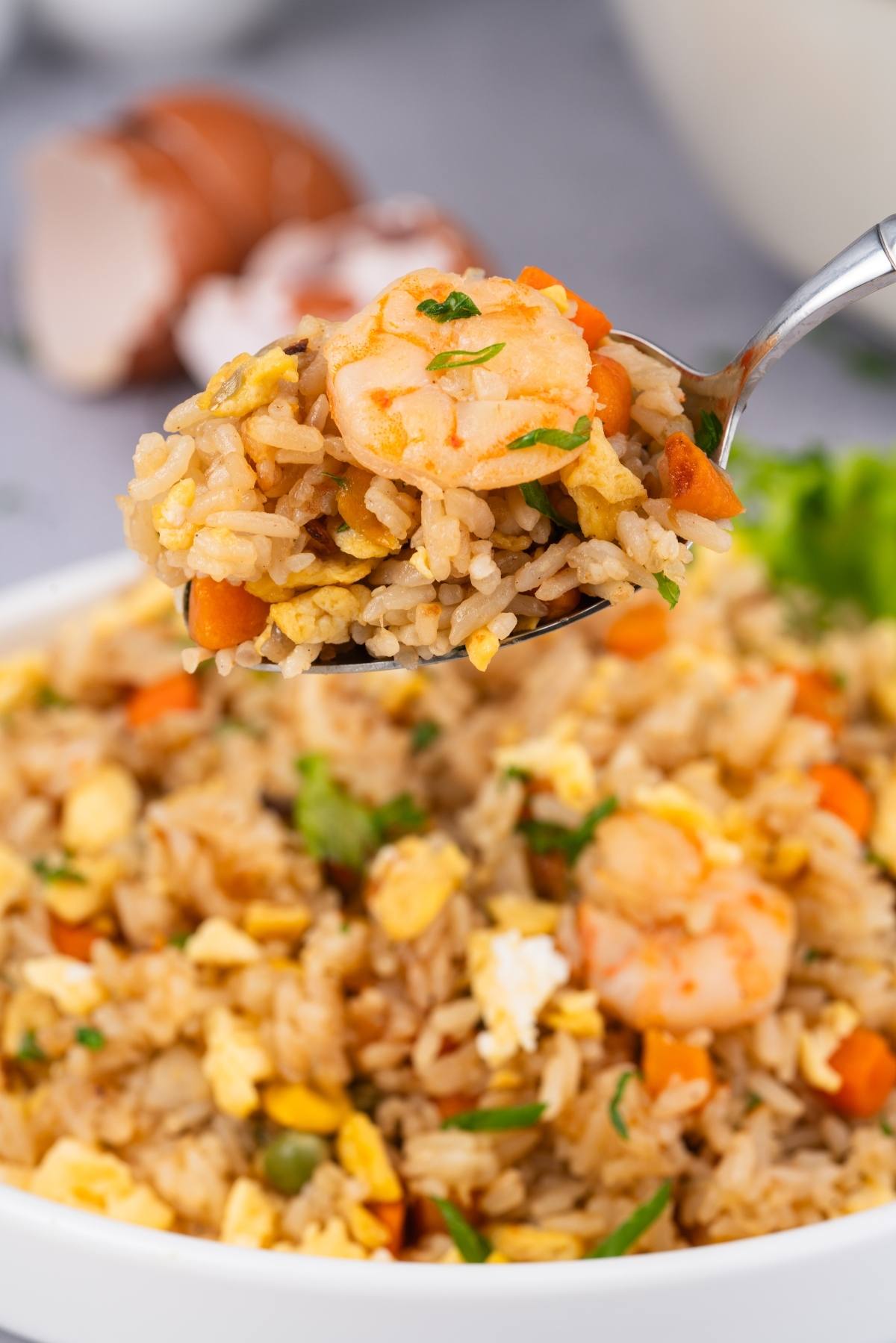 A spoonful of shrimp fried rice with egg, carrots, and herbs held above a bowl of the same dish.