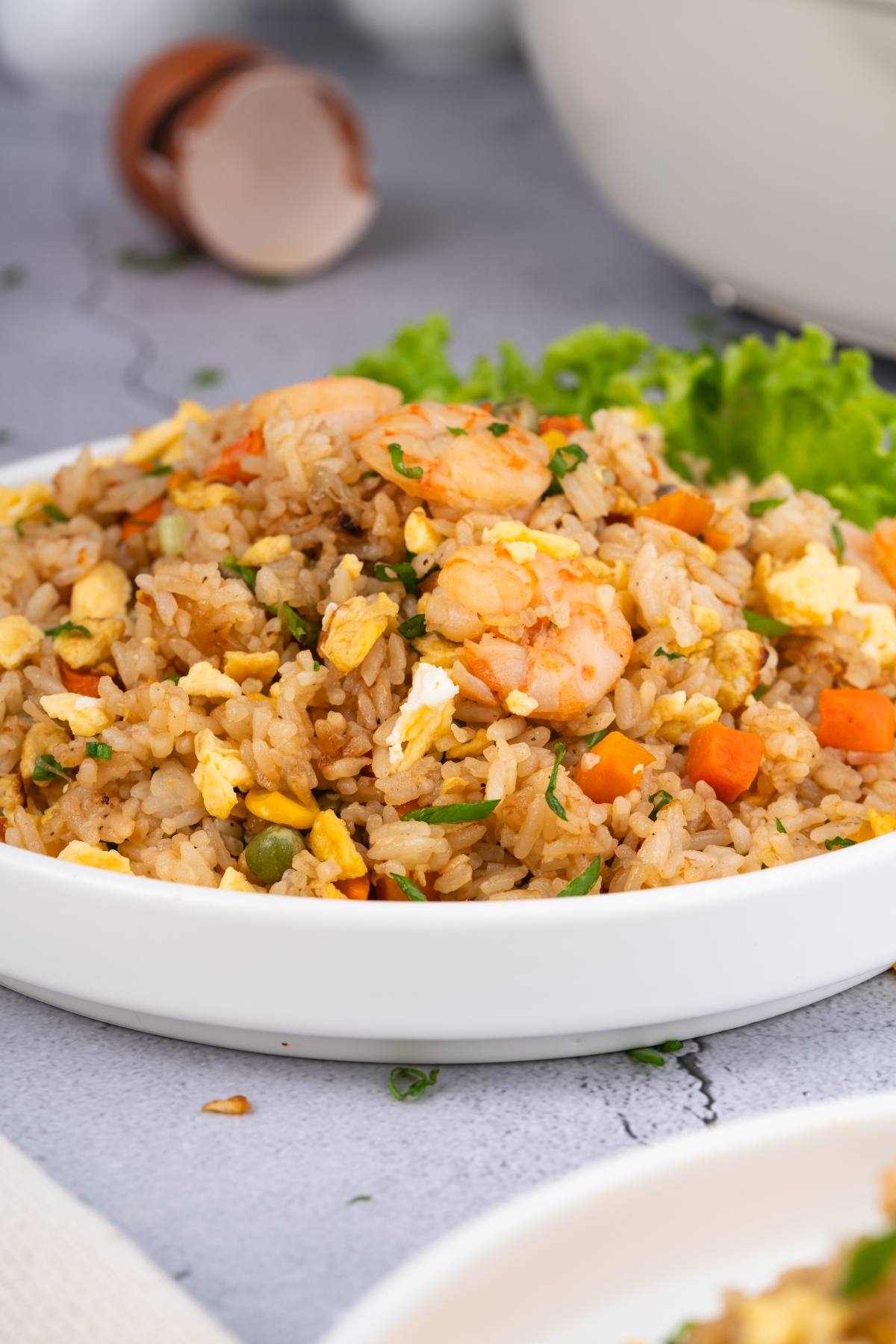 A plate of shrimp fried rice with vegetables and scrambled eggs, garnished with lettuce on the side.