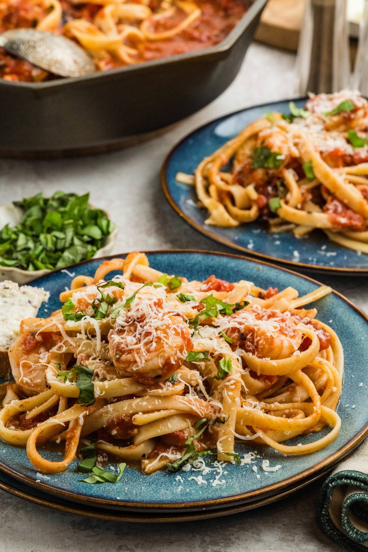 Two plates of Shrimp fra diavolo  pasta with tomato sauce, grated cheese, and fresh herbs, served on a table.