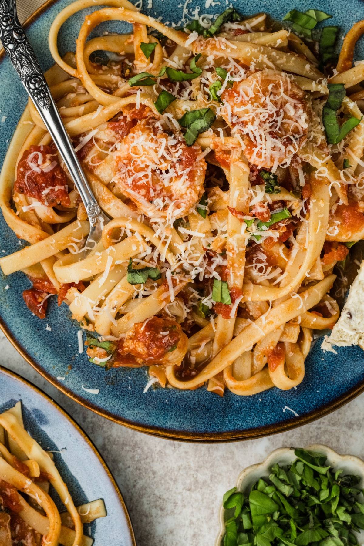 A plate of Shrimp fra diavolo pasta with tomato sauce, grated cheese, fresh basil, and a fork.