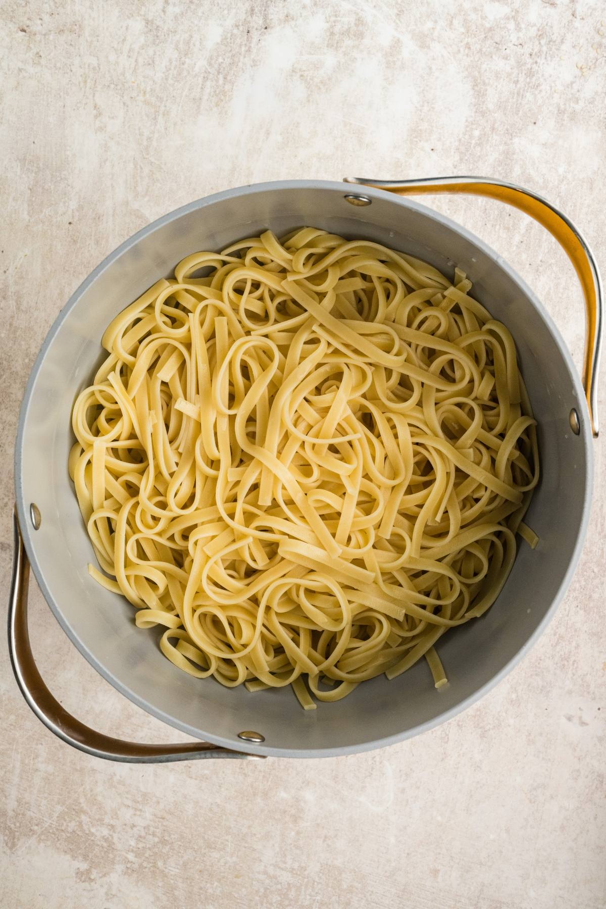 A pot of cooked linguine pasta rests on a light-colored surface.