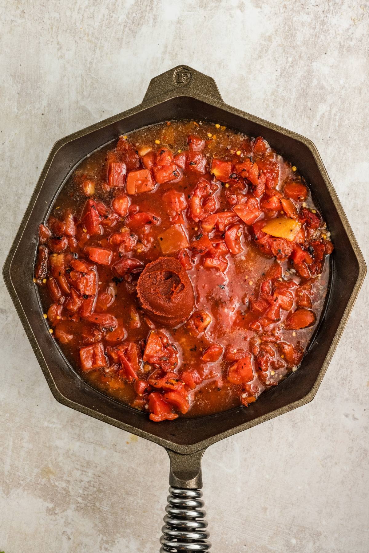 A pan filled with chopped tomatoes and tomato paste cooking in sauce on a light surface.