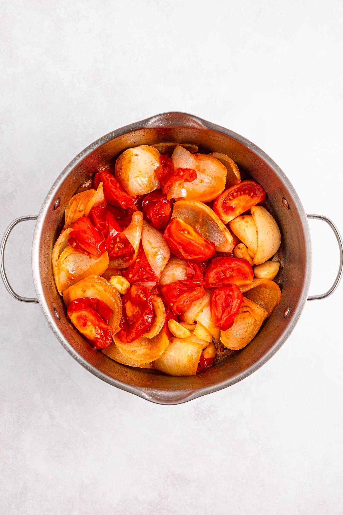 Chopped tomatoes, onions, and garlic in a metal pot, ready to be cooked.