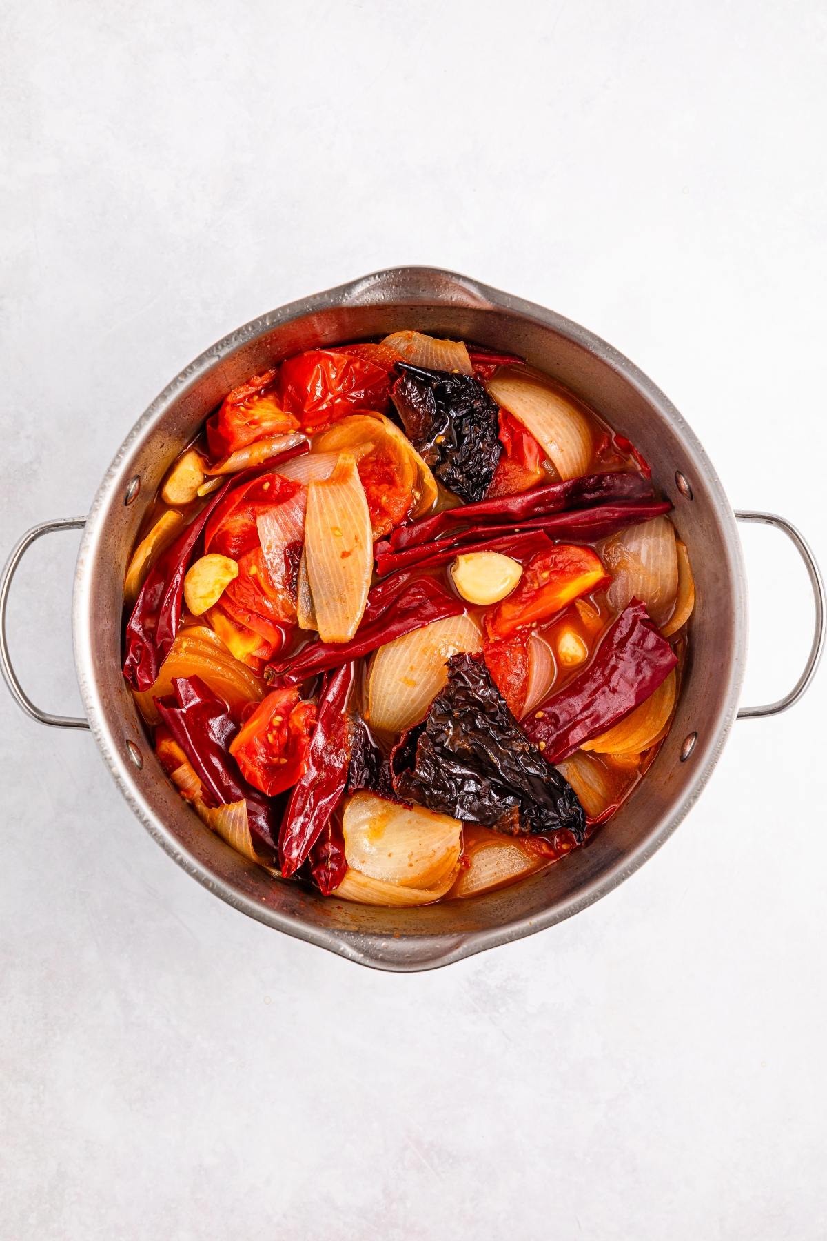 A pot filled with tomatoes, onions, garlic, and dried chilies simmering in broth.