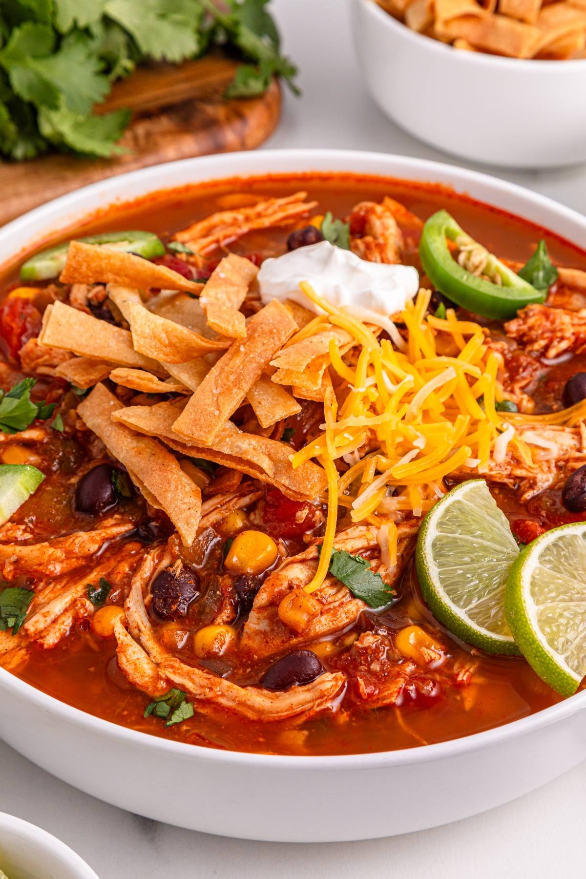 Bowl of chicken tortilla soup with shredded cheese, sour cream, tortilla strips, and lime wedges on top.