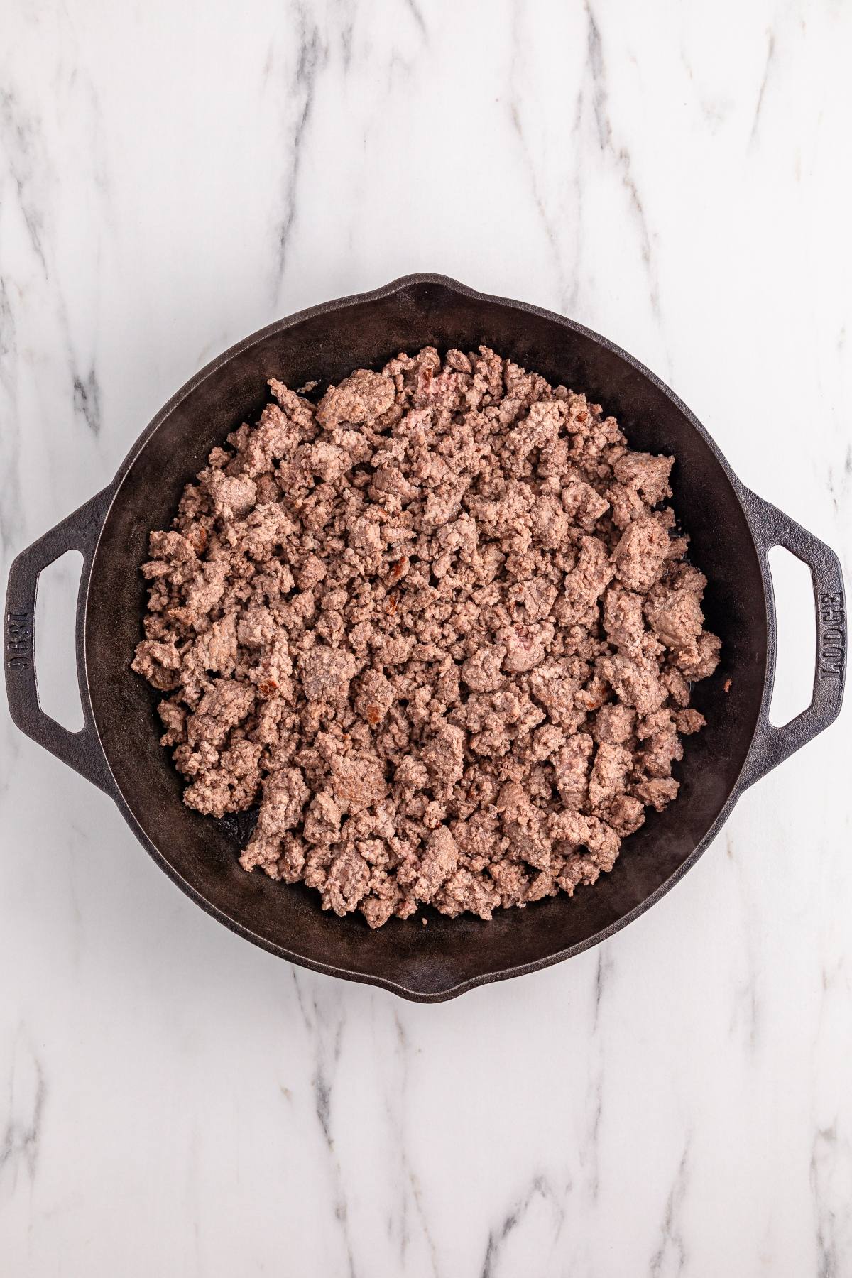 Cooked ground beef in a cast iron skillet on a white marble surface, viewed from above.